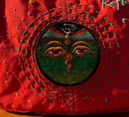 Close-up of the hand-embroidered eyes and running stitch on the red shoulder bag
